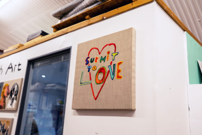 A photograph of an embroidered artwork saying "Submit to love" with a love heard behind it
